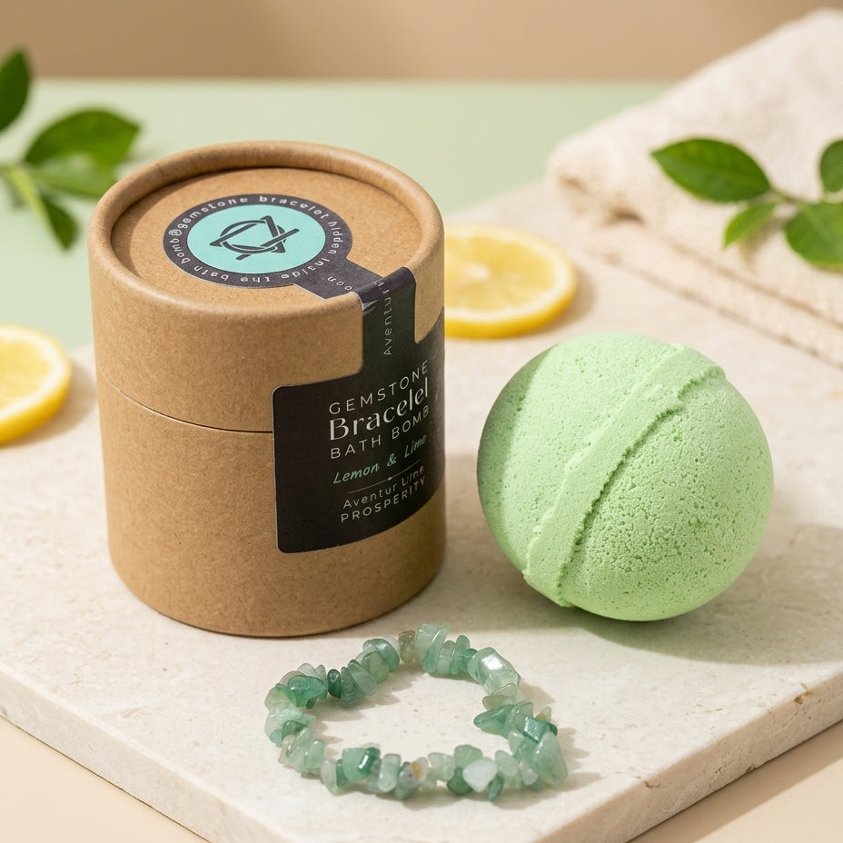 A light green gemstone bath bomb and matching faceted bracelet displayed beside a kraft paper cylindrical package labeled 'Gemstone Braceloo Bath Bomb' on a marble slab with lemon slices and a folded towel in the background.