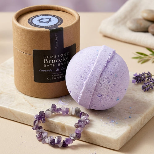 A lavender gemstone bracelet bath bomb and its kraft paper packaging cylinder, styled on a marble slab with a matching gemstone bracelet and lavender sprigs.