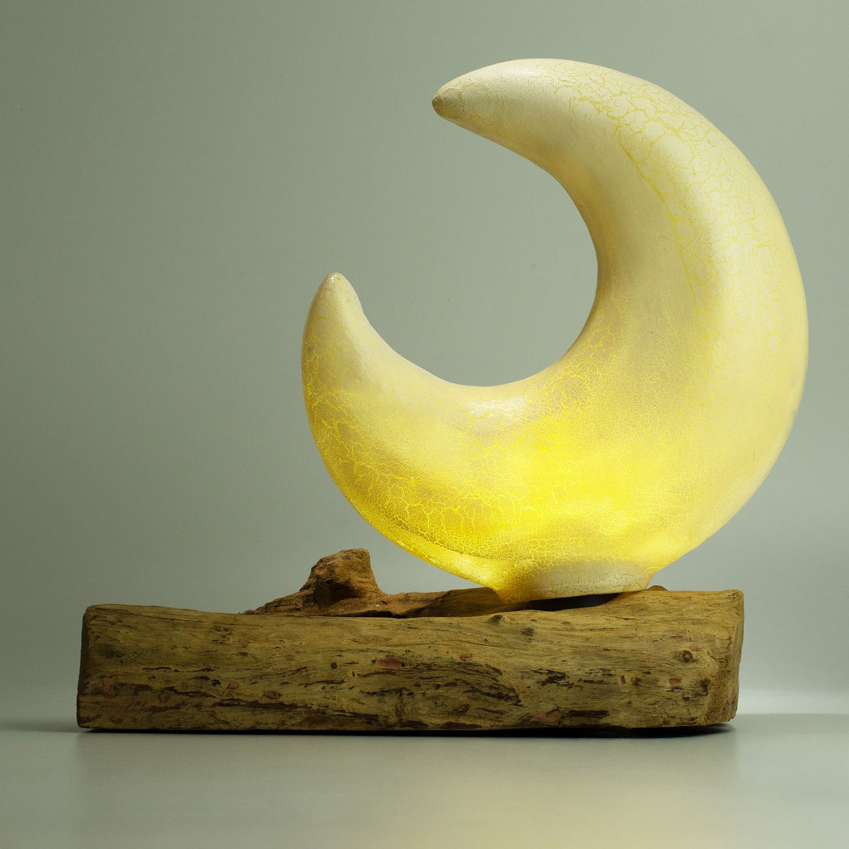 Glowing moon-shaped light fixture on a wooden base against a neutral background