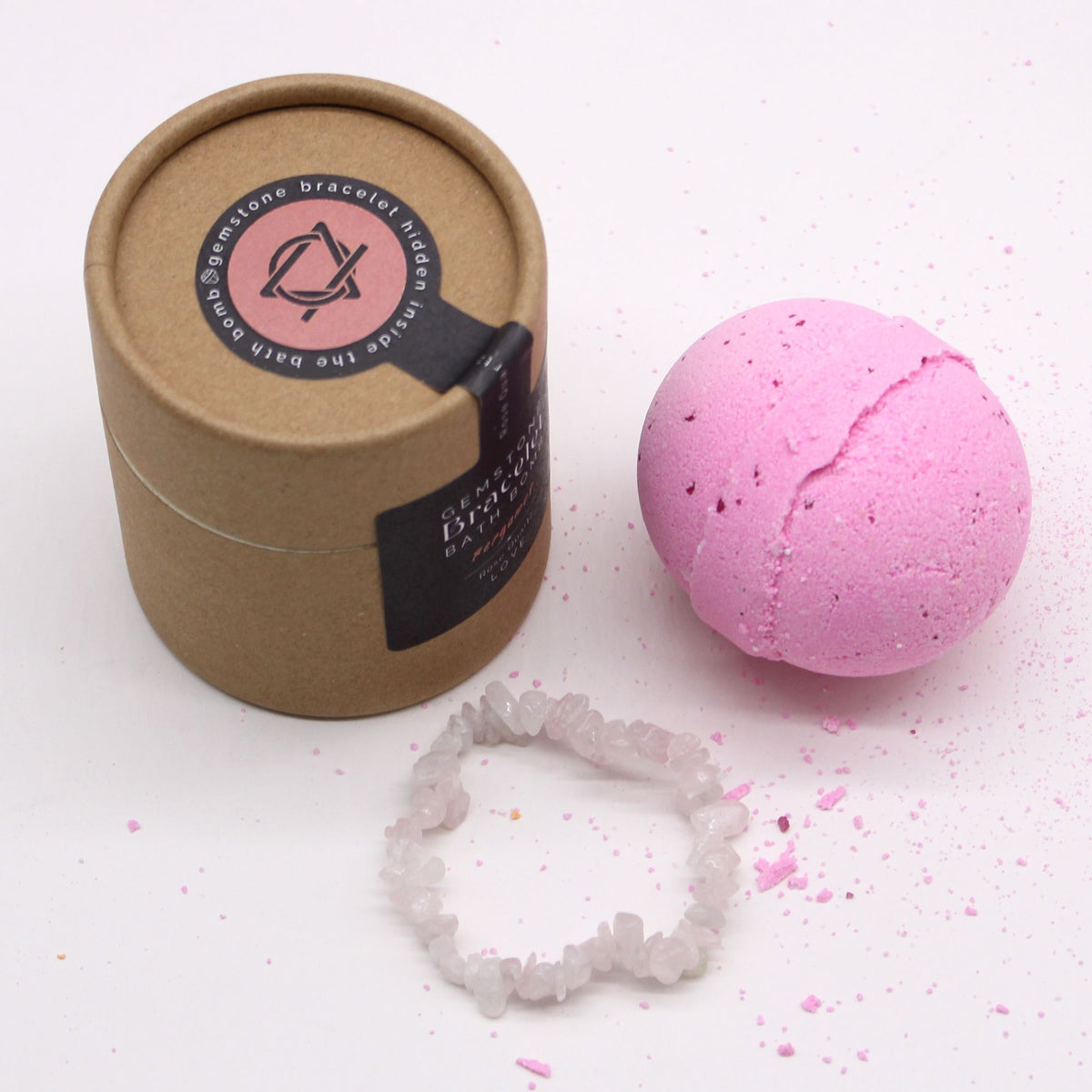 Pink bath bomb with a brown paper container and crystal bracelet on a white background