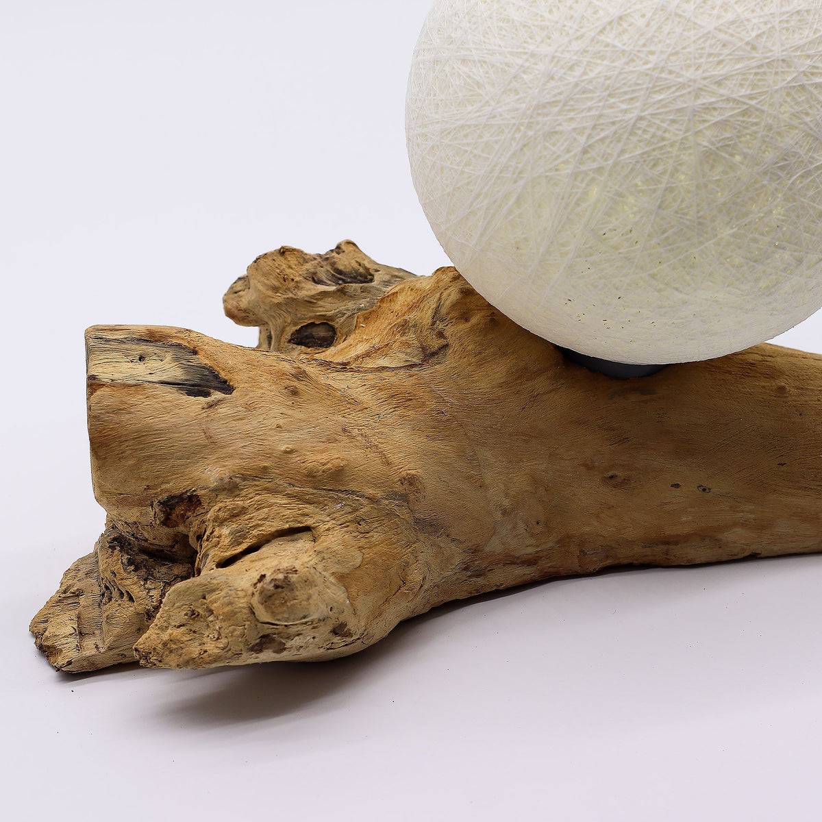 White ball of yarn on a piece of driftwood against a white background