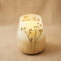 Candle in a textured ceramic holder with dried flowers on a beige background