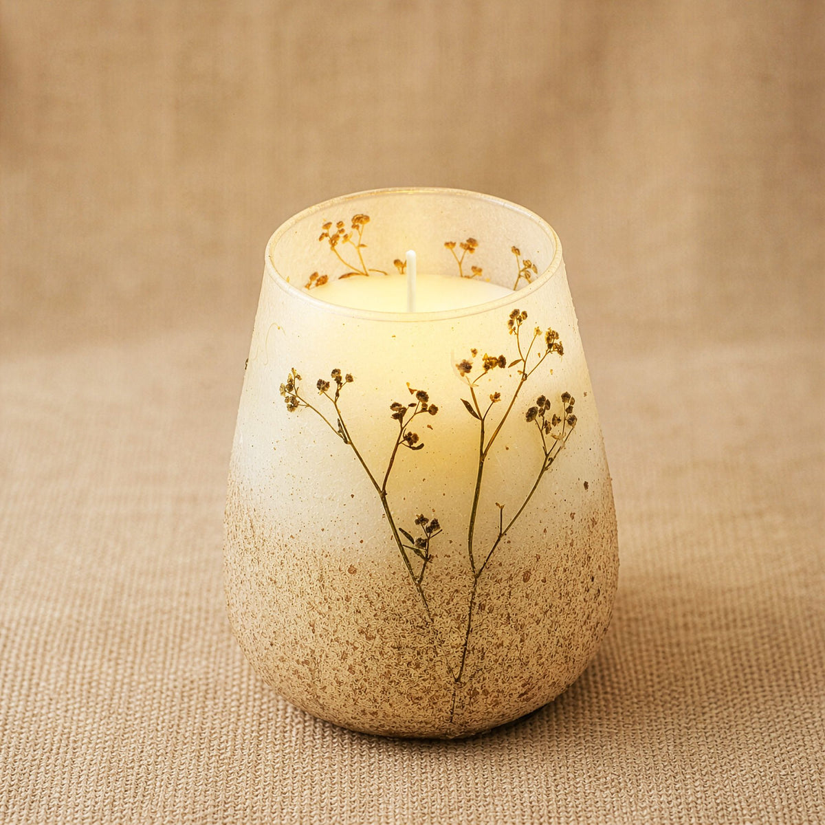 Candle in a textured ceramic holder with dried flowers on a beige background
