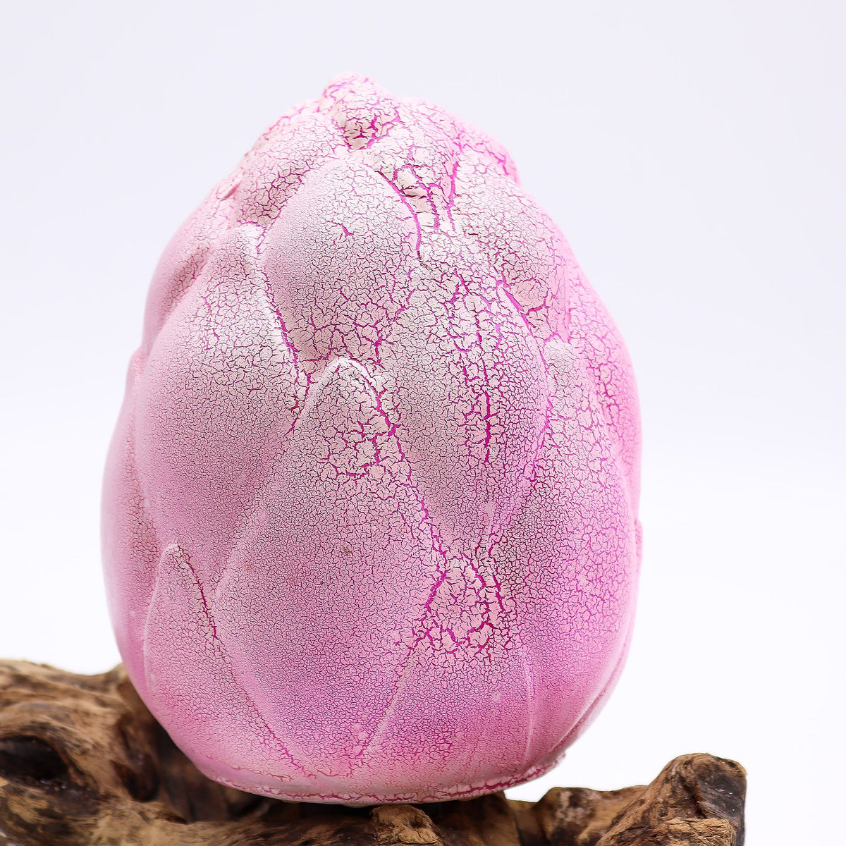 Pink textured object resembling a cracked egg on a wooden surface with a light purple background